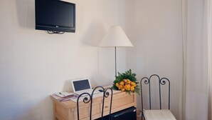 A small room with a desk, a chair, a TV, a lamp, and a bouquet of flowers. - S'Arenada Hotel (Villasimius)