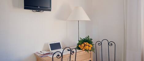 A small room with a desk, a chair, a TV, a lamp, and a bouquet of flowers.