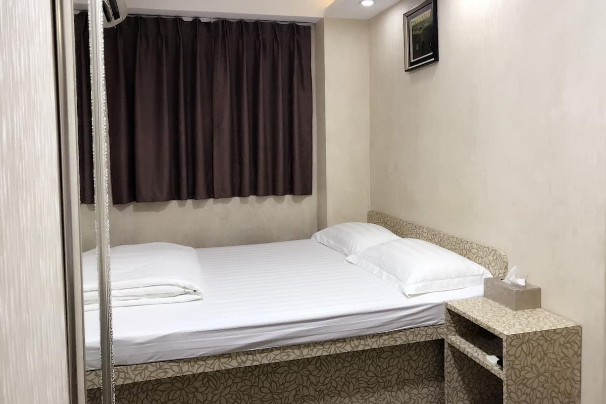 A neatly made bed with white linens, a dark brown curtain, a small bedside table with a tissue box, and a framed picture on the wall.