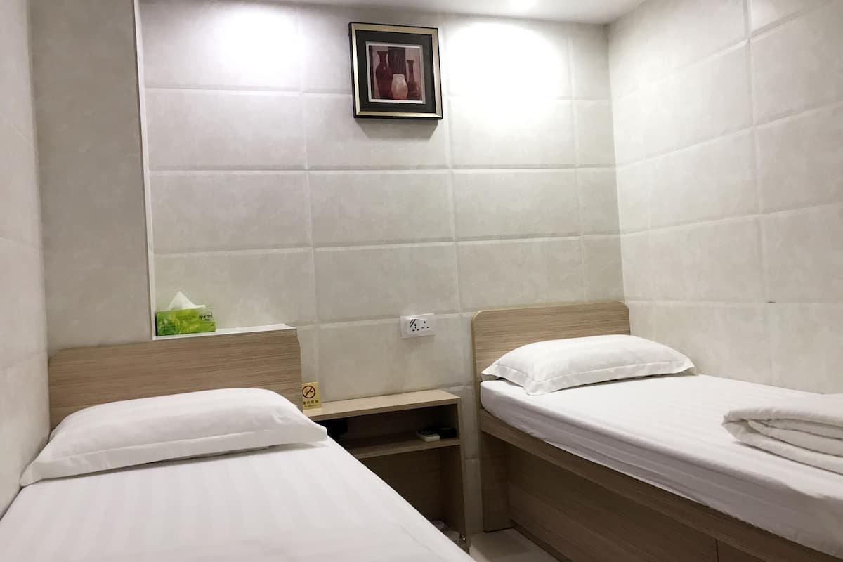 A small, clean room with two single beds, a nightstand, a framed picture on the wall, and a small shelf with a tissue box.