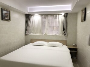 Een slaapkamer met een bed, nachtkastje, raam met gordijnen en een plafondlamp.