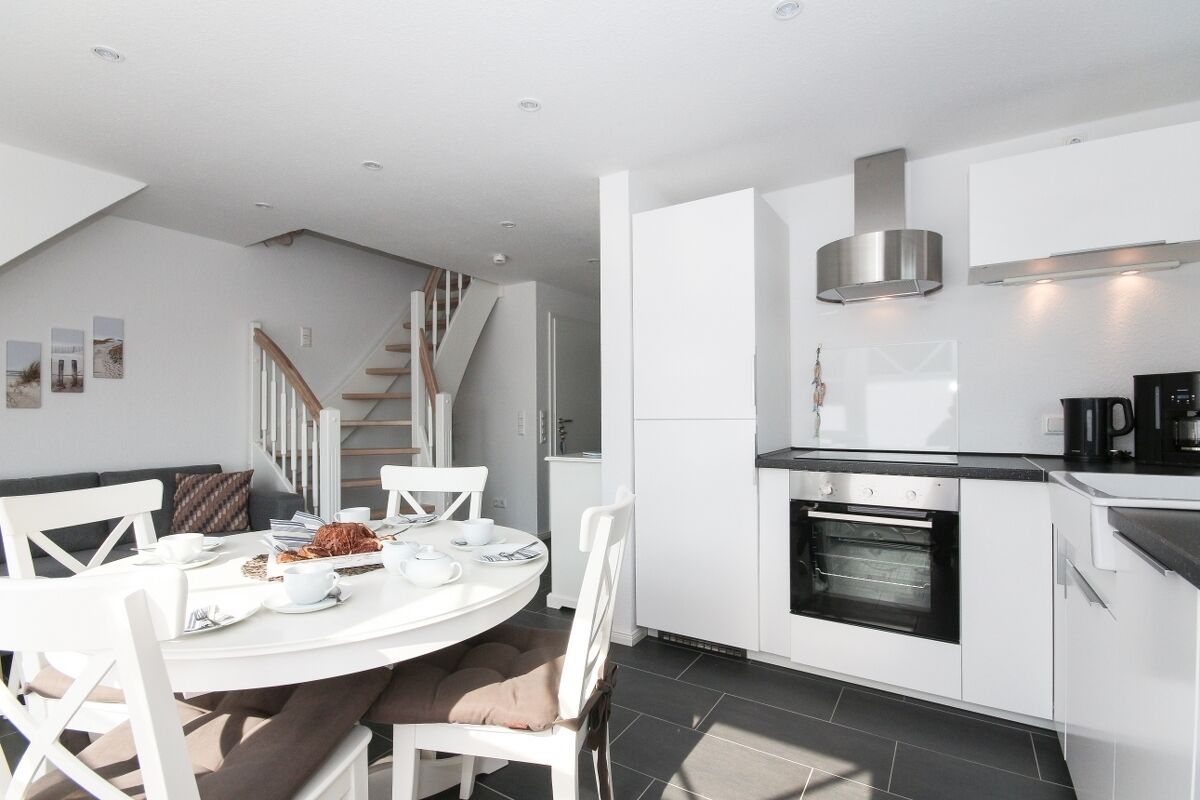 Cocina moderna con muebles blancos, horno empotrado y escalera que sube a un nivel superior.