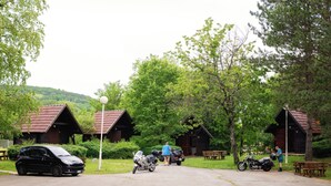 A row of rustic cabins with a paved driveway, surrounded by lush greenery and trees. - Kamp Korana (Rakovica)