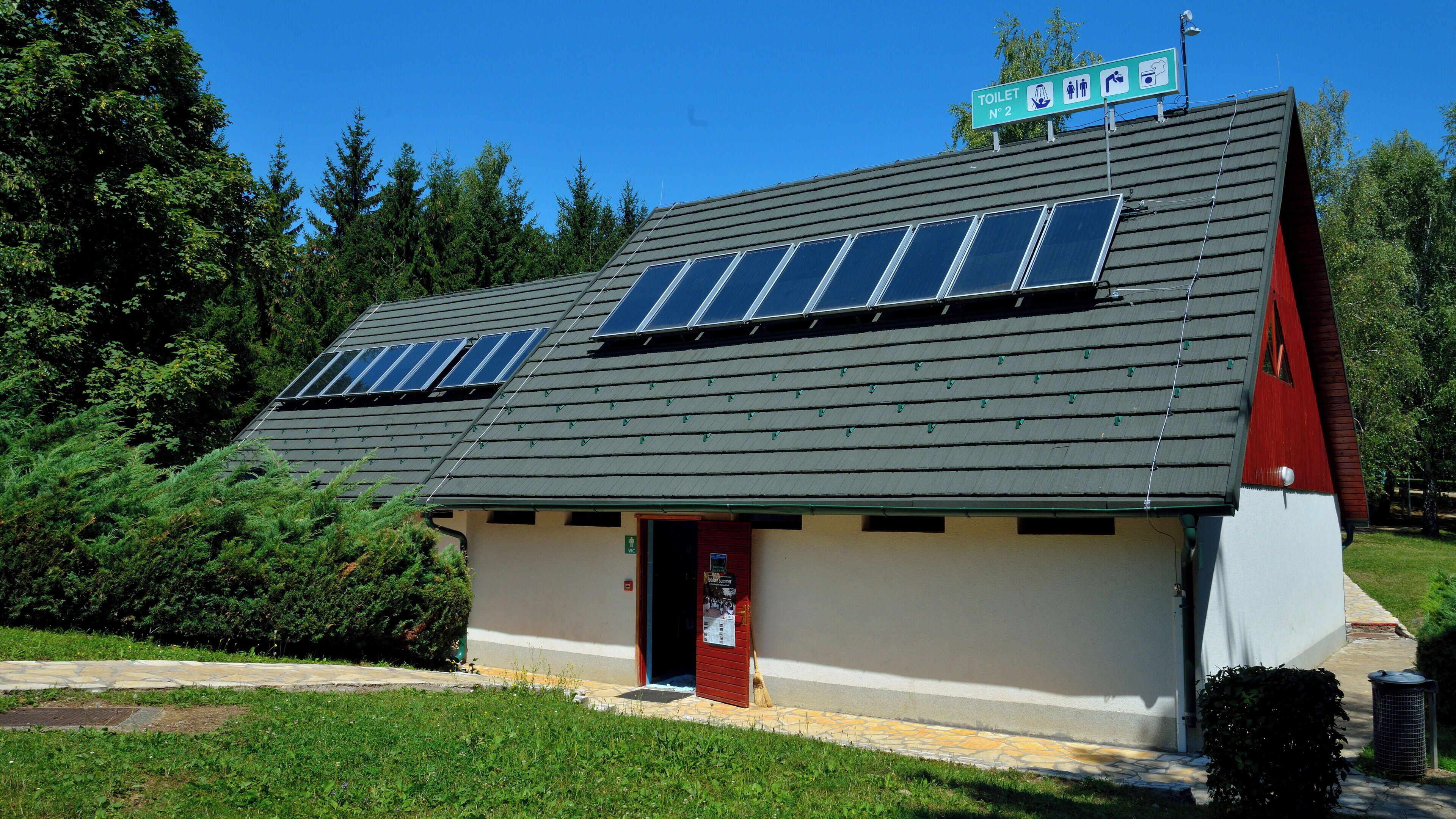 A building with a sloped roof, solar panels, and a sign indicating a toilet.