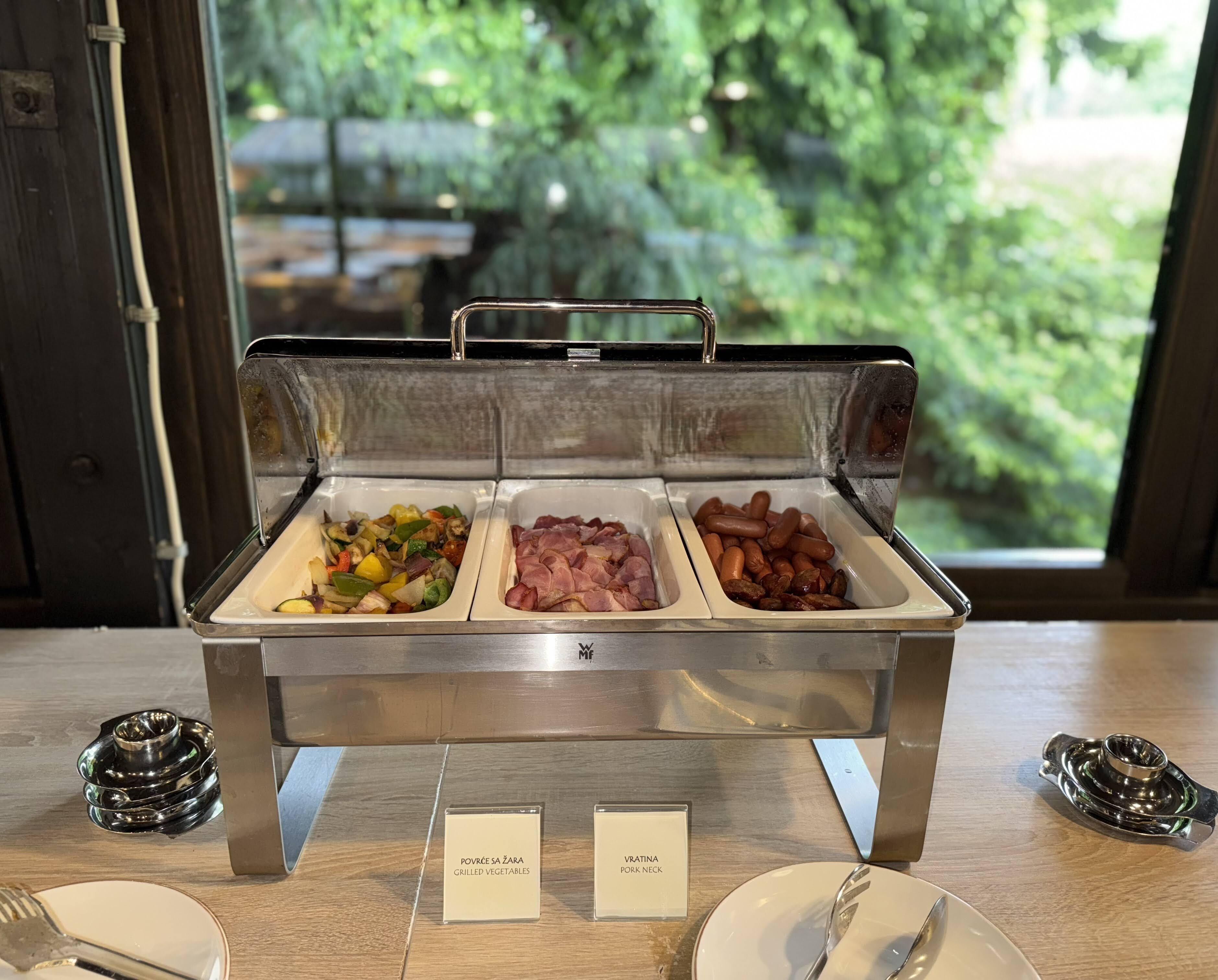 Een buffet met aangeduide secties voor gegrilde groenten en varkensnek.