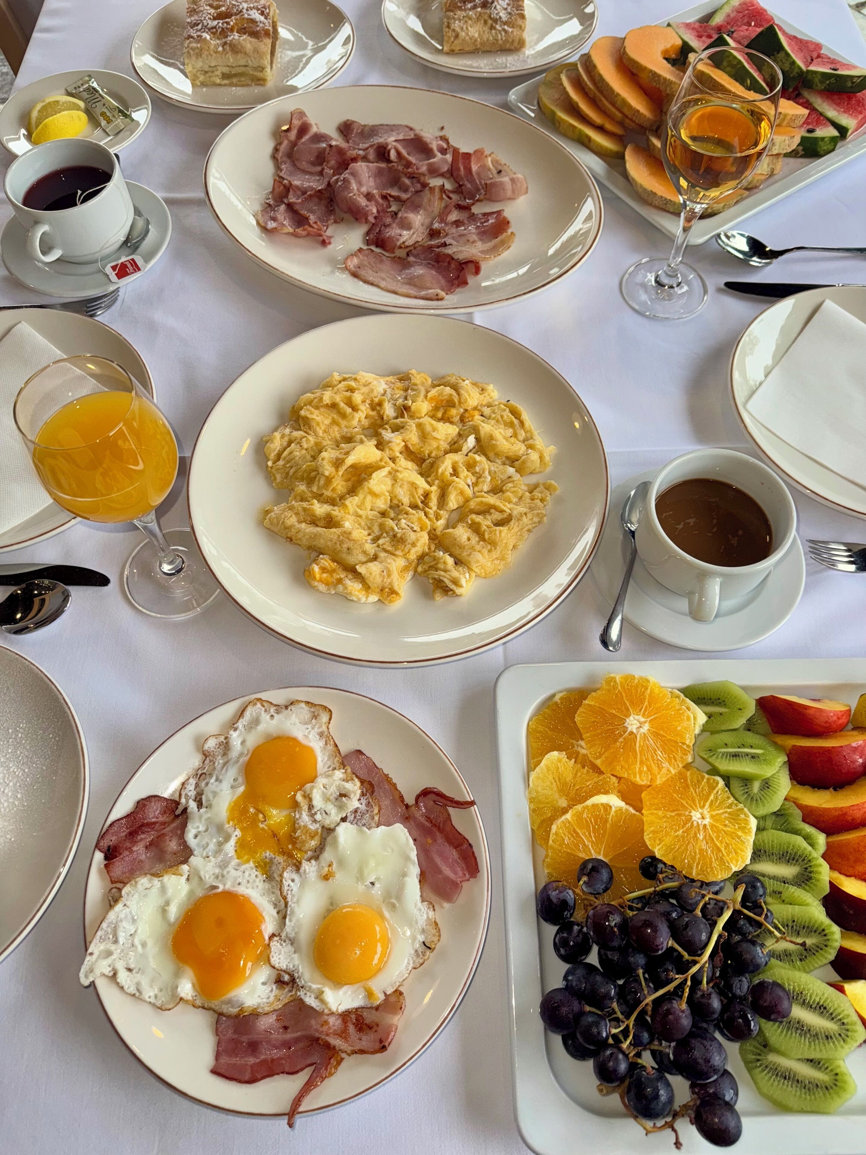 Desayuno con huevos revueltos, tocino, tostadas con huevo y una bandeja de fruta.