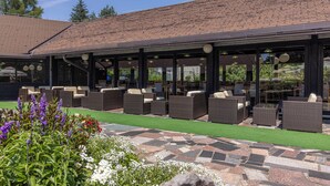 An outdoor seating area with wicker furniture and a patio with artificial turf and stone tiles. - Kamp Korana (Rakovica)
