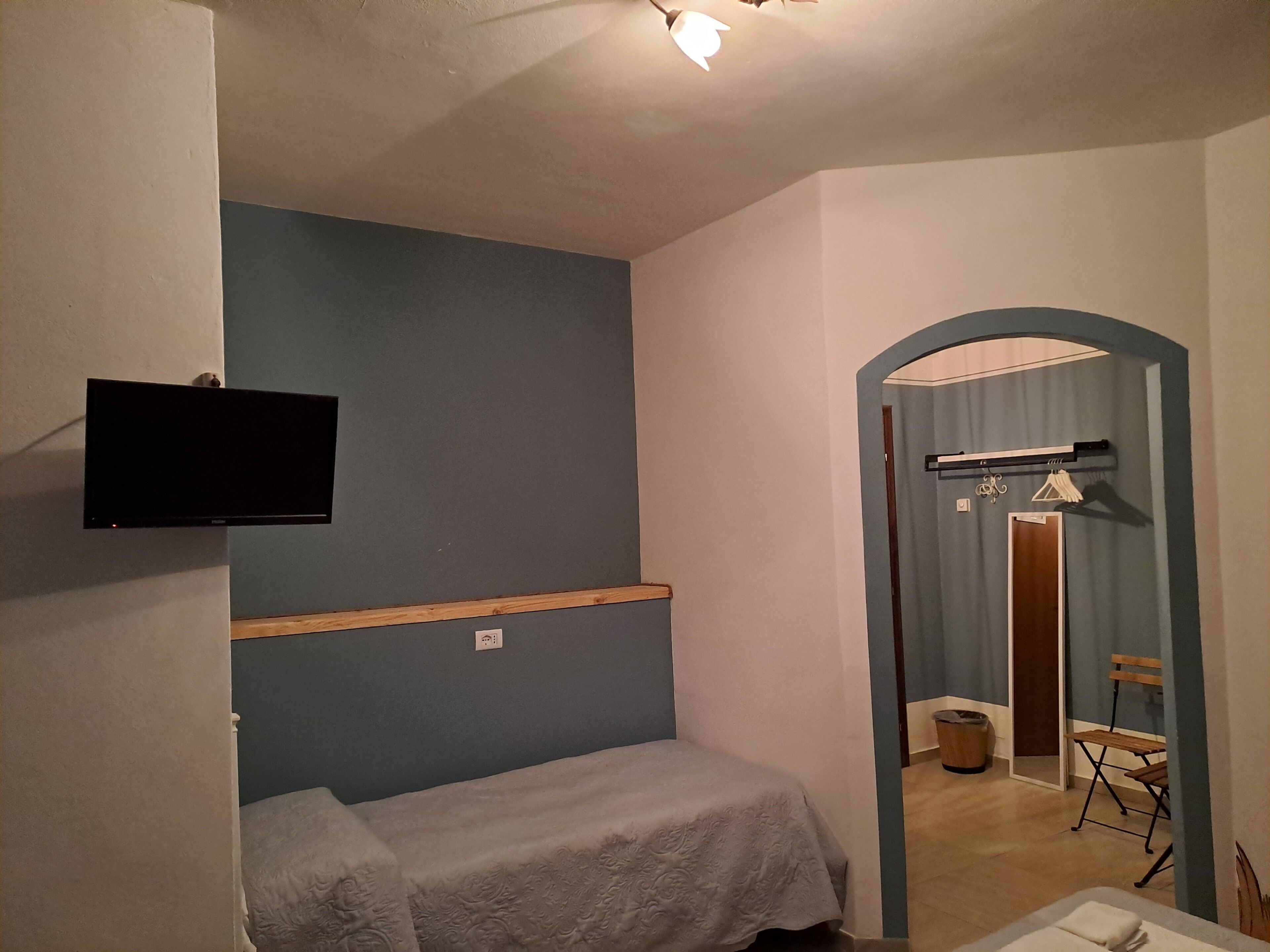 A small, simple room with a bed, a mounted television, and a door leading to a bathroom.