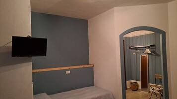 A small, simple room with a bed, a mounted television, and a door leading to a bathroom.