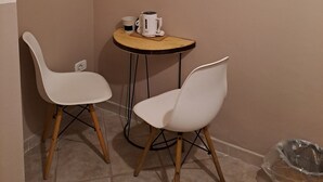 Een kleine kamer met twee witte stoelen, een ronde tafel met een koffiezetapparaat, en een lijst aan de muur.