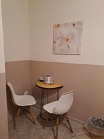 Una habitación pequeña con dos sillas blancas, una mesa redonda con una cafetera y un cuadro en la pared.