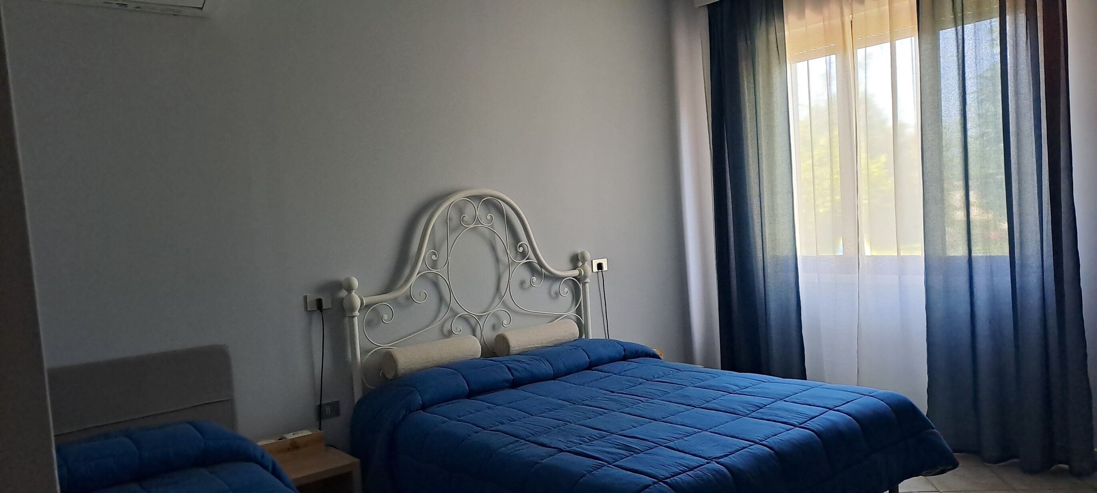 Un dormitorio con cama, mesita de noche y ventana con cortinas.