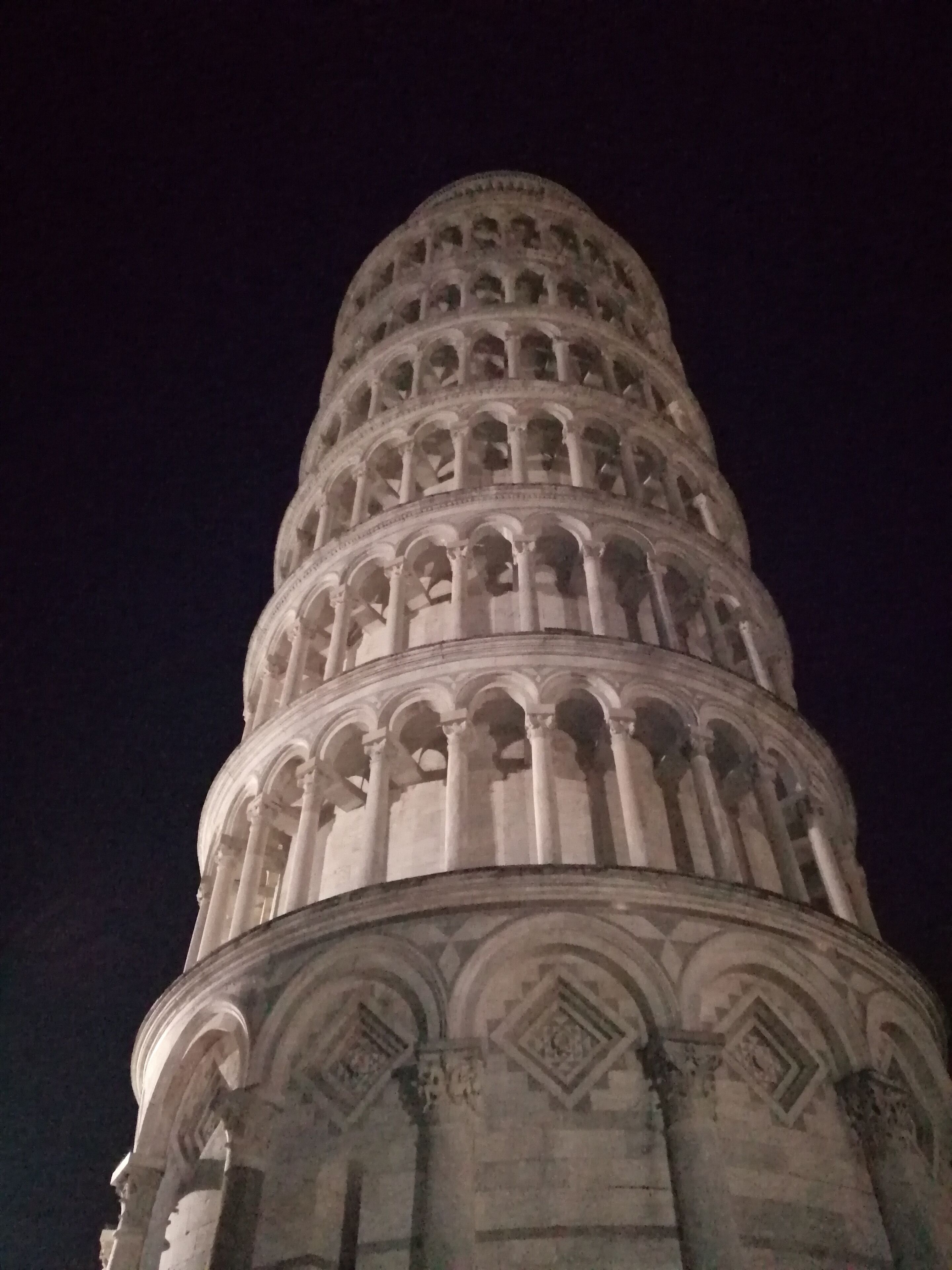 Ein historischer Turm mit mehreren Geschoßen aus Bögen und Säulen, beleuchtet bei Nacht.