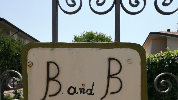 Een bord met de tekst 'Band B Villa Oasi' bevestigd aan een metalen poort.