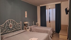 Een hotelkamer met twee bedden, een klein nachtkastje met een lamp, een stoel en een raam met gordijnen.