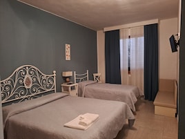 Habitación de hotel con dos camas, una mesita de noche con lámpara, una silla y un ventanal con cortinas.