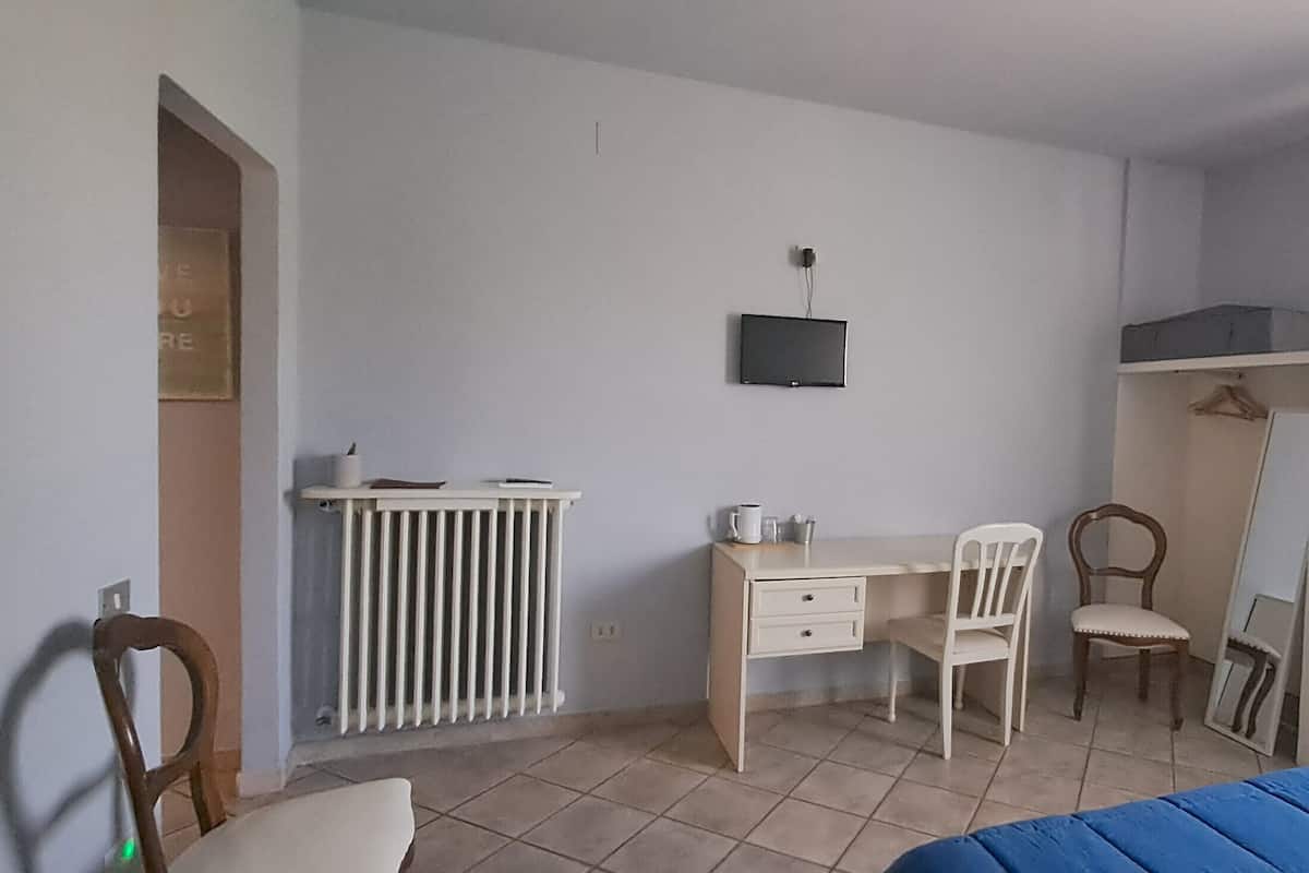 Une chambre à coucher comprenant un lit, un bureau, une chaise, un radiateur, une armoire et un téléviseur.