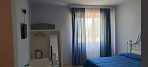 Un dormitorio con cama, escritorio, silla, armario y ventana con cortinas.