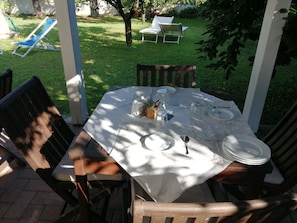 Une terrasse extérieure avec une table dressée pour quatre personnes, entourée de chaises en bois, dans un coin ensoleillé du jardin.
