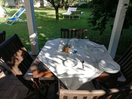 Un patio al aire libre con una mesa lista para cuatro personas, rodeada de sillas de madera, en un jardín soleado.