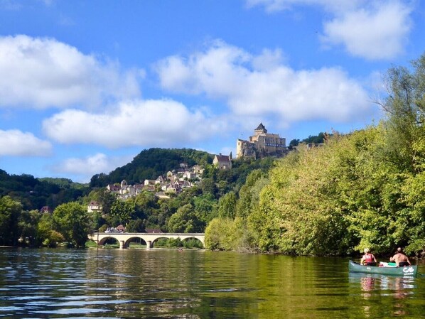 Un castillo histórico en una colina con vistas a un río, un puente y abundante vegetación.