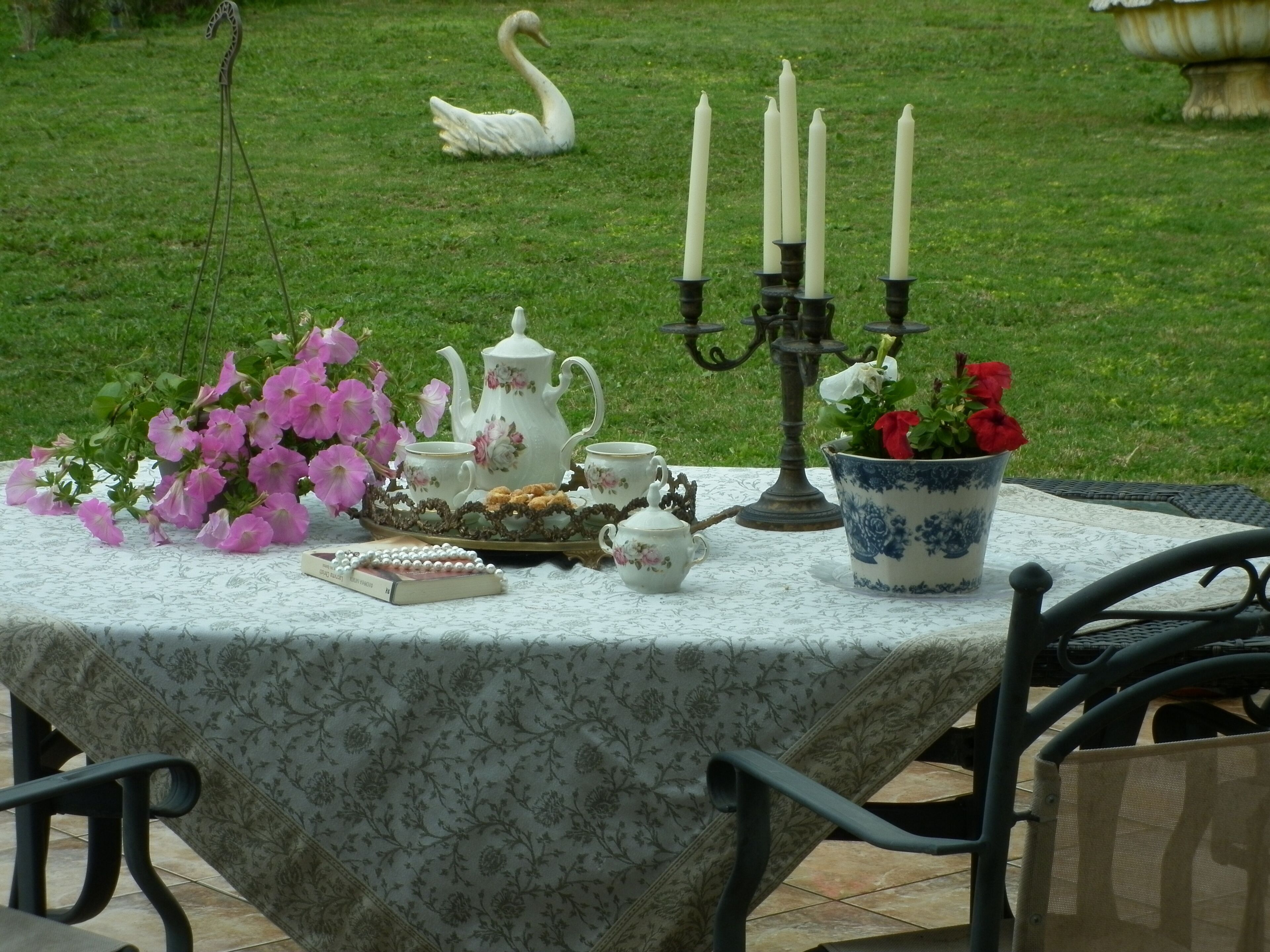 A table set with a floral tablecloth, a teapot, cups, a book, and a vase with flowers.