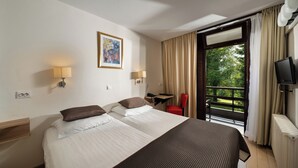 A hotel room with two beds, a desk, a chair, a TV, and a window with curtains.