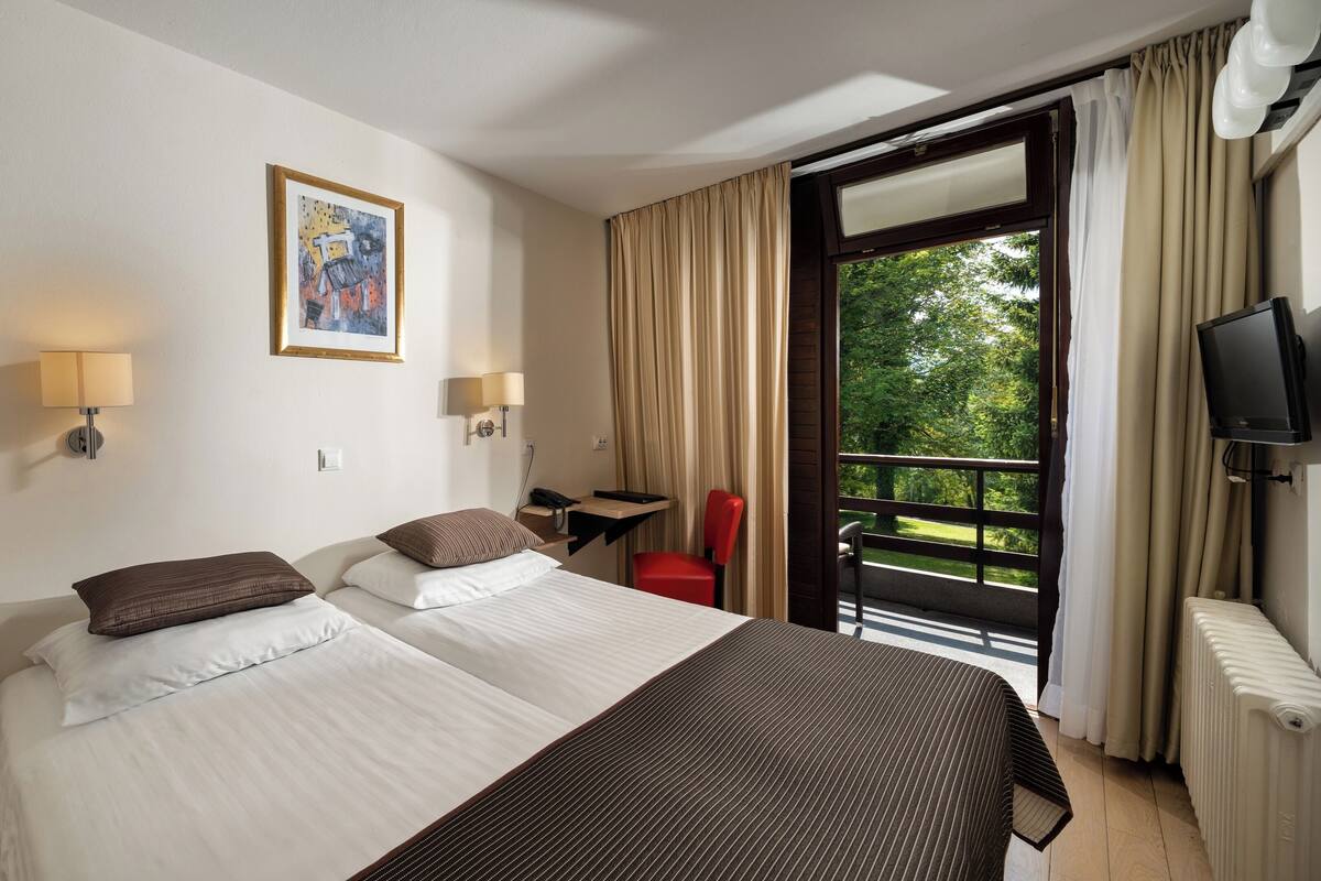 A hotel room with two beds, a desk, a chair, a TV, and a window with curtains.