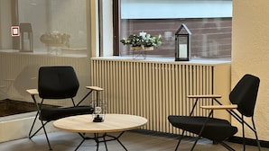 A room with a round table and two black chairs, a small potted plant, and a window with blinds.