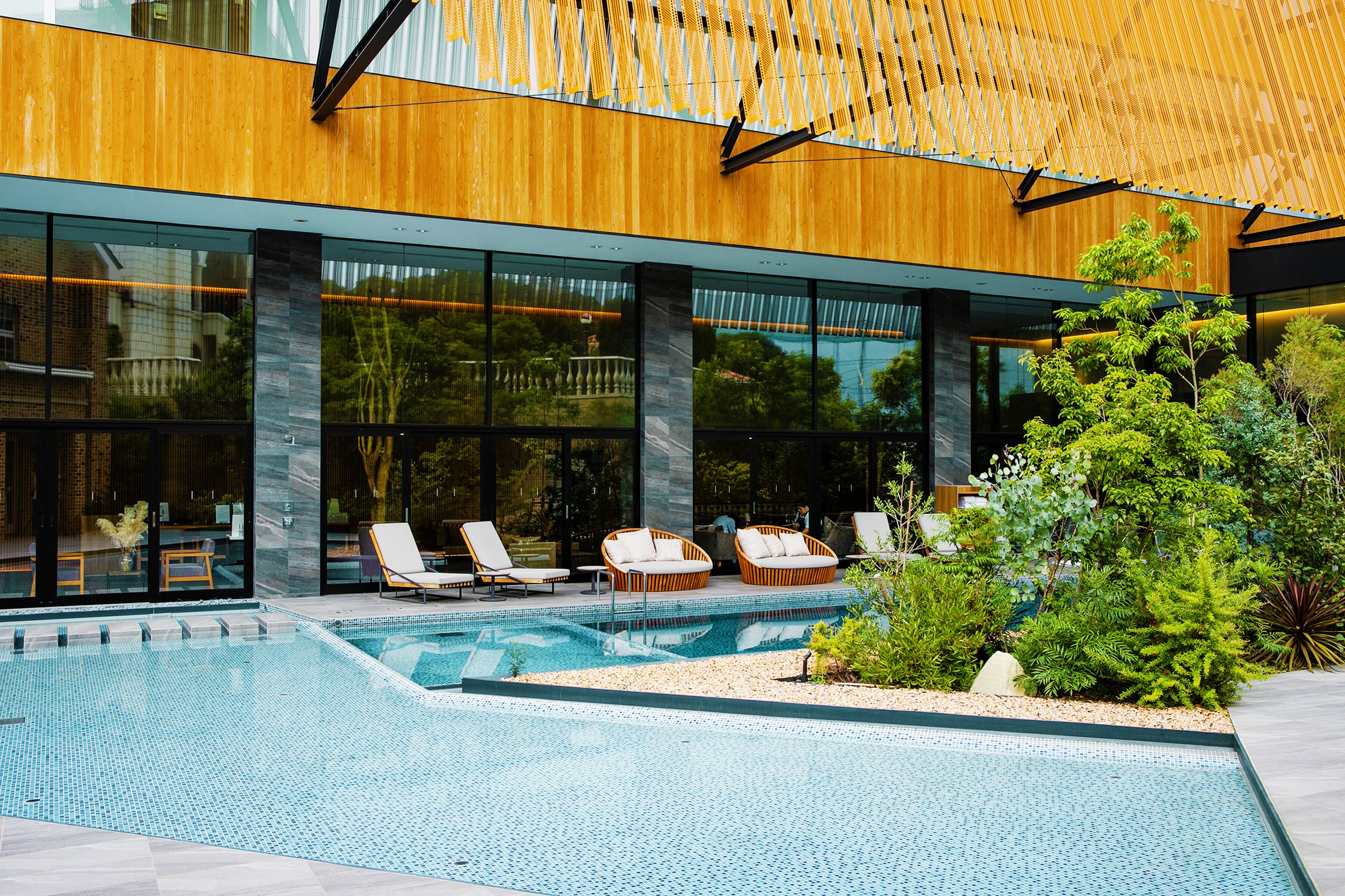 Uma área de piscina moderna ao ar livre, com espreguiçadeiras e um pérgola de madeira.