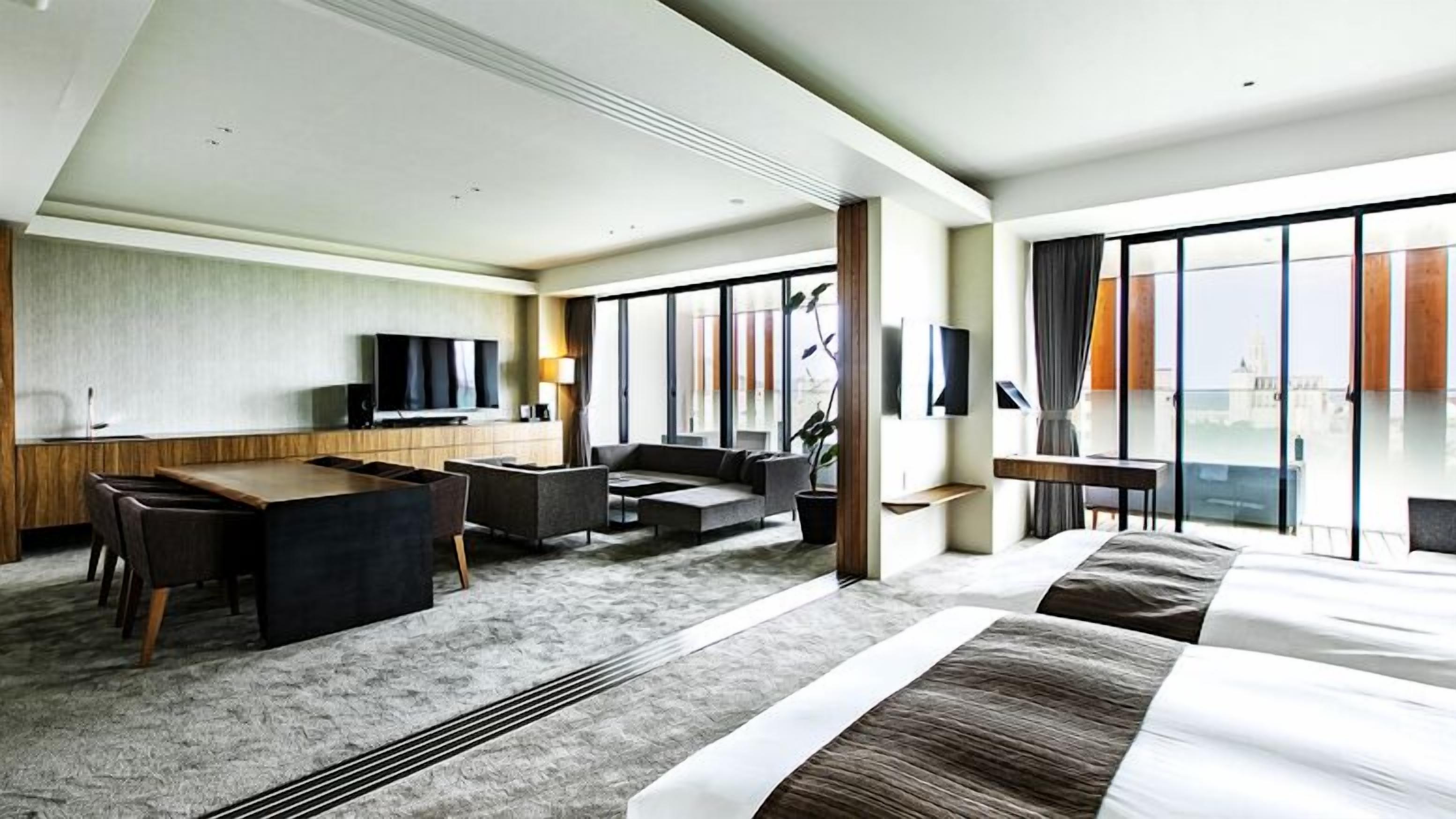 A hotel room with a bed, a desk, a sofa, a TV, and large windows.