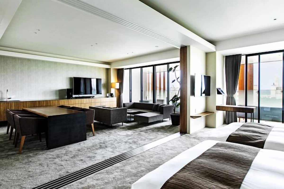 Habitación de hotel con cama, escritorio, sofá, televisión y ventanas amplias.