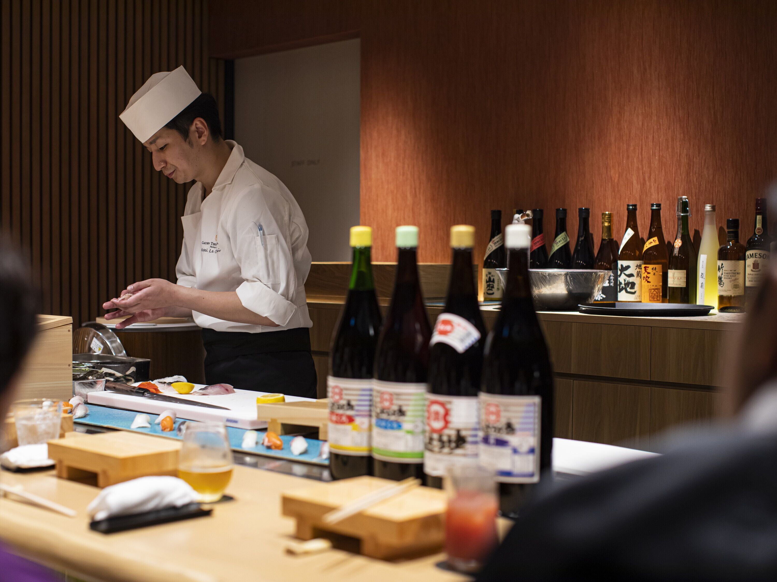 A chef preparing food in a restaurant with a variety of bottles and condiments on the counter.