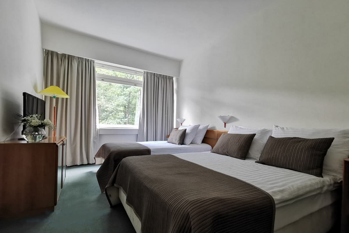 A hotel room with two beds, a desk, a lamp, and a window with curtains.