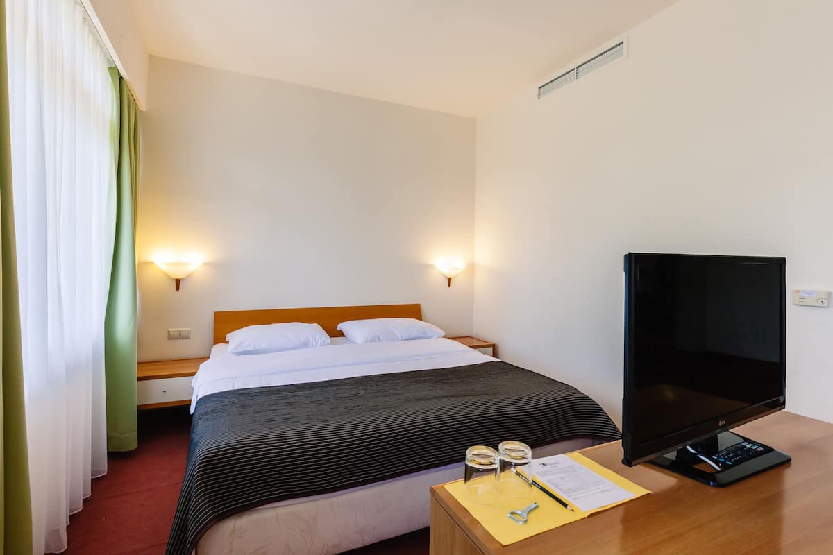 A hotel room with a bed, bedside table, TV, and a desk with a computer.