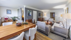 A modern living room with a wooden dining table, grey sofas, and a TV.