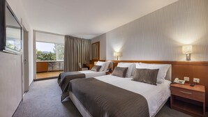 Quarto de hotel com duas camas, varanda e vista para o verde.