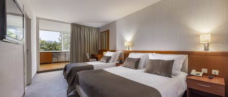 A hotel room with two beds, a balcony, and a view of greenery.