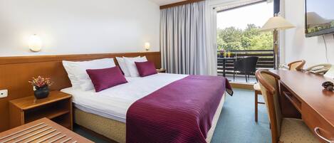 Una habitación de hotel con cama, mesita de noche, lámpara y un escritorio con silla.
