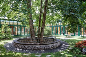 A circular stone and brick garden with a metal railing, surrounded by trees and a building with glass doors and green frames. - Hotel Jezero Plitvice Lakes (Plitvicka Jezera)