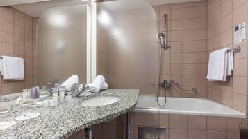 A bathroom with a granite countertop, a sink, a mirror, a shower with a handheld showerhead, and two towels hanging on hooks.