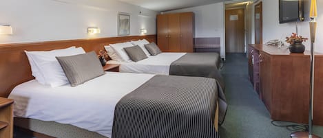 A hotel room with two beds, a wooden wardrobe, a desk with a lamp, and a television mounted on the wall.