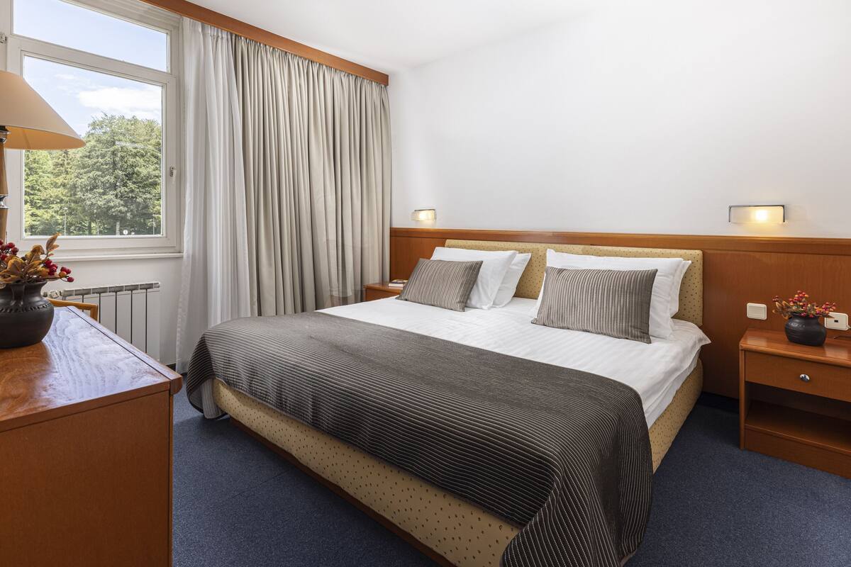 Une chambre d’hôtel avec un lit, une table de chevet, une lampe et une fenêtre avec des rideaux.