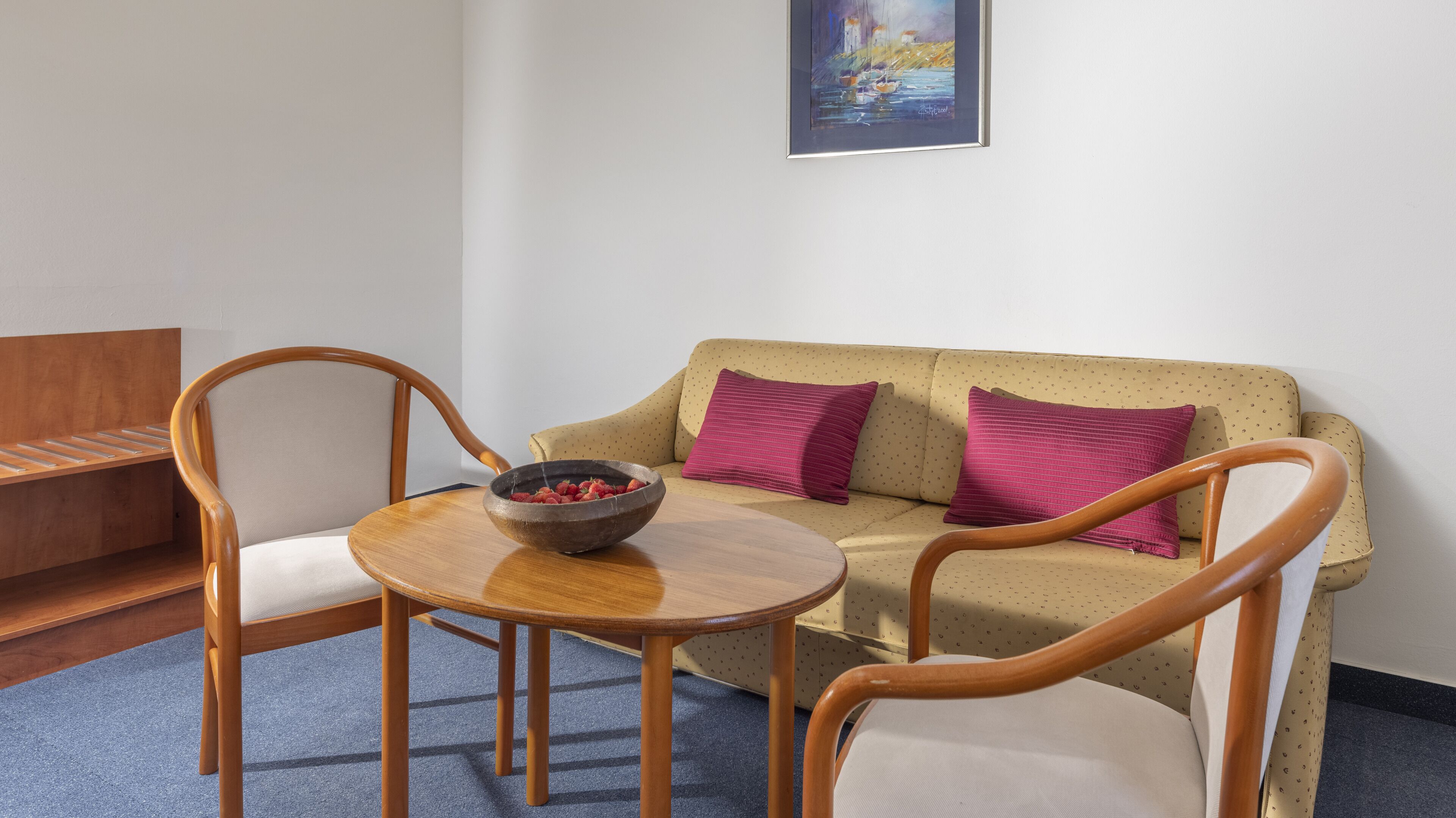 Una habitación acogedora con un sofá, dos sillas de madera, una mesita redonda y un cuenco de fruta.