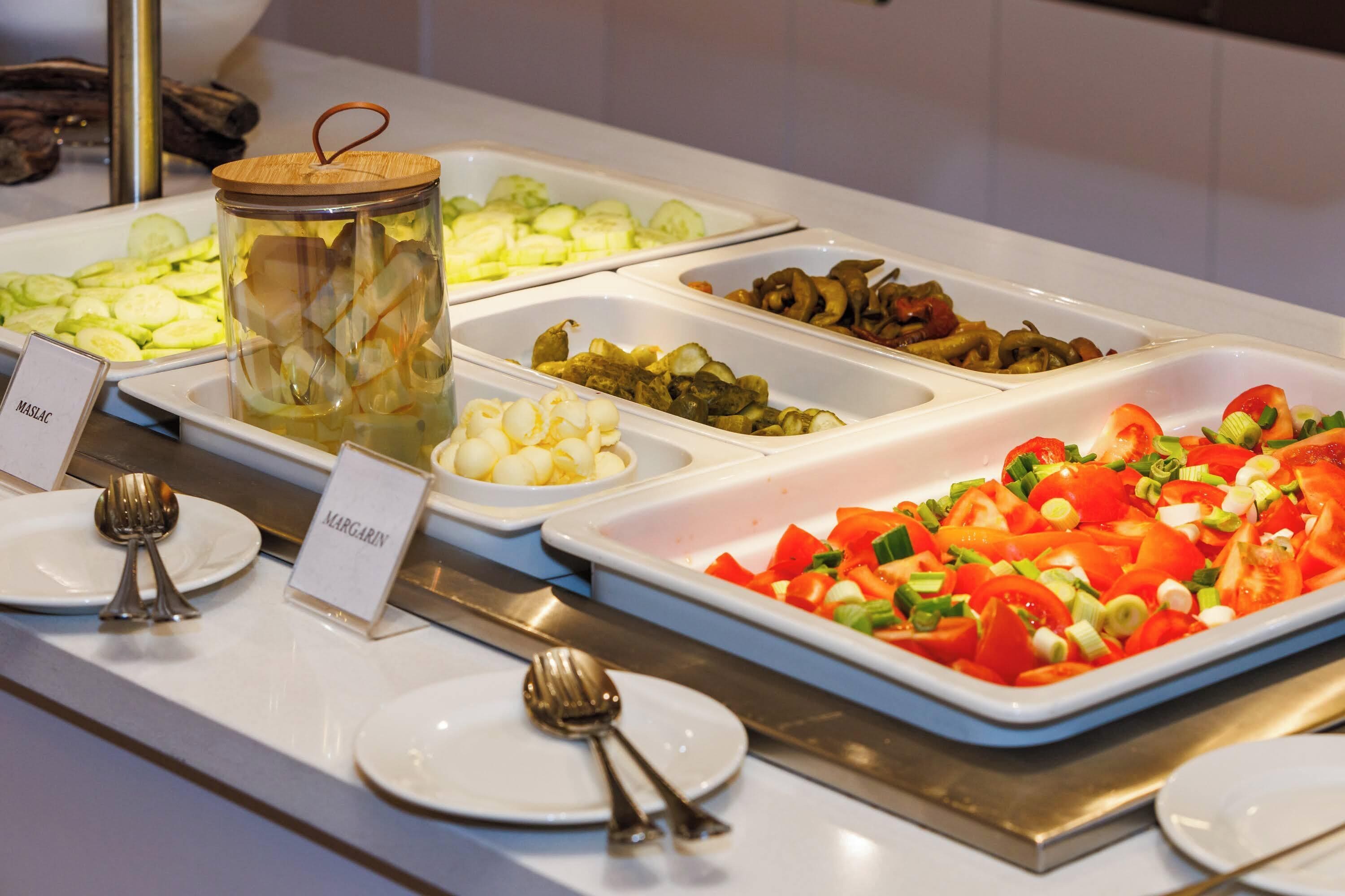 A buffet with various food options including sliced cucumbers, mushrooms, and a tomato salad.