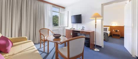 Una habitación de hotel con sofá, una mesa de comedor con sillas, un escritorio con computadora, televisor y lámpara.