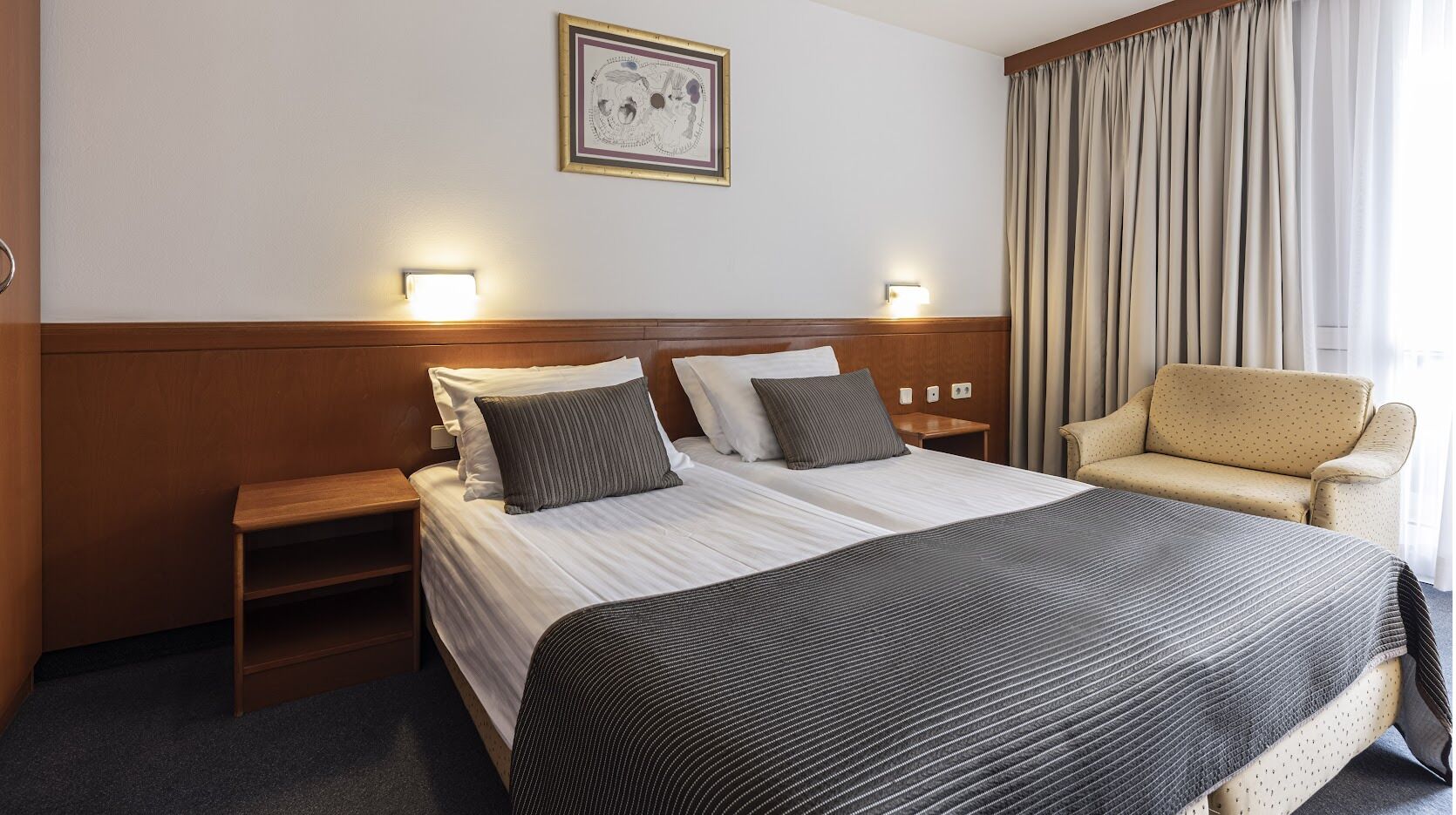 Een hotelkamer met een groot bed, twee nachtkastjes, een stoel en een aan de muur hangend schilderij.