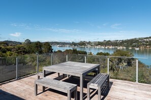 A wooden deck with a table and benches overlooking a lake with boats. - The Tide Watcher - Okiato Holiday Home (Okiato)