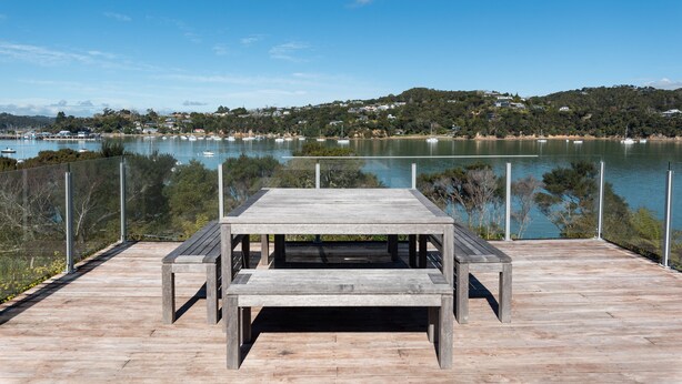 A wooden deck with a picnic table overlooking a lake with boats and houses in the background. - The Tide Watcher - Okiato Holiday Home (Okiato)