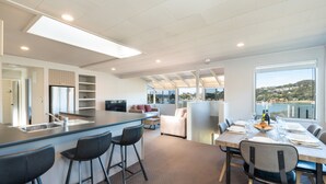 A modern kitchen with a bar area, seating for dining, and a view of the outdoors. - The Tide Watcher - Okiato Holiday Home (Okiato)